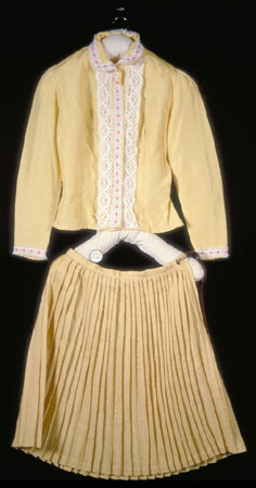 Partie d'un costume confectionné pour être porté par des enfants lors de danses et de pièces, cette blouse de fabrication commerciale est faite d'un tissu synthétique jaune, dotée de longues manches et ornée de dentelle blanche et de rubans à motif floral., © MCC/CMC, 77-251.1
