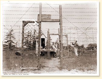 After supper a bugle call announces that the gate is open for fishing or a walk along the river. Here the camp spokesmen watch the signing-out and will see that every man returns. They post their own sentries outside to see that no one wanders. - AN19830444-052 - Canadian Army Photo 2907-1