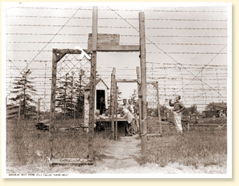 After supper a bugle call announces that the gate is open for fishing or a walk along the river. Here the camp spokesmen watch the signing-out and will see that every man returns. They post their own sentries outside to see that no one wanders. - AN19830444-052 - Canadian Army Photo  2907-1