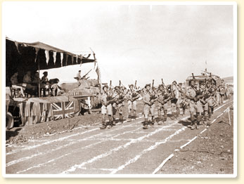 Les cornemuseurs du 48th Highlanders of Canada, une unité d'infanterie de Toronto (Ont.), divertissent l'assistance présente à une rencontre d'athlétisme pendant une période de repos durant la bataille de la Sicile, 23 août 1943. - Photo : Armée canadienne - No 23196, CWM Reference Photo Collection