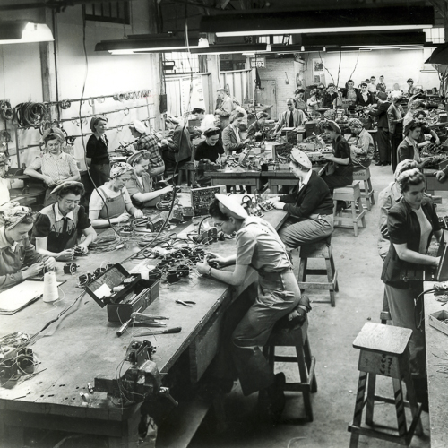 Women on a factory floor wearing head scarves or hats.