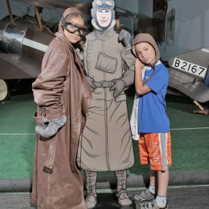 Two kids dress up as pilots and pose with a cutout of a cartoon pilot.