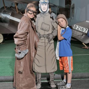 Two kids dress up as pilots and pose with a cutout of a cartoon pilot.