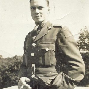 A black and white photograph of a man in uniform holding a cigarette and looking at the camera