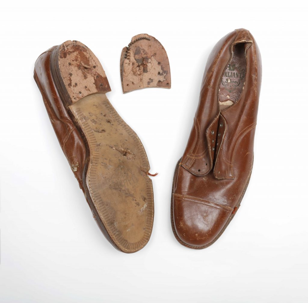 Two brown leather shoes, one of which is upside down, showing a damaged sole and detached heel