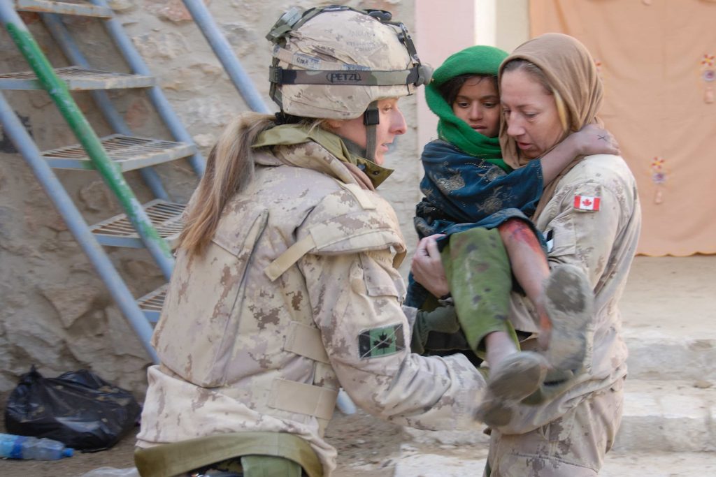 A uniformed woman carries an Afghan child in her arms, while another uniformed woman assists.