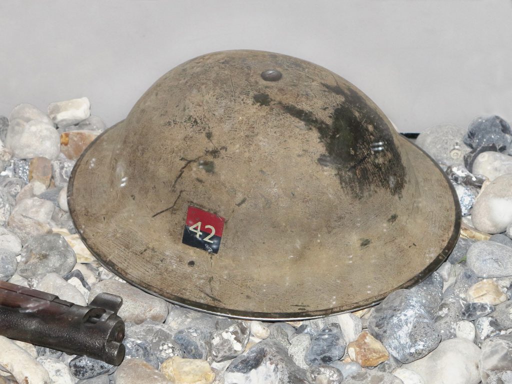 A worn Mark II helmet with a small painted badge on the side consisting of the number 42 on a red and black square.