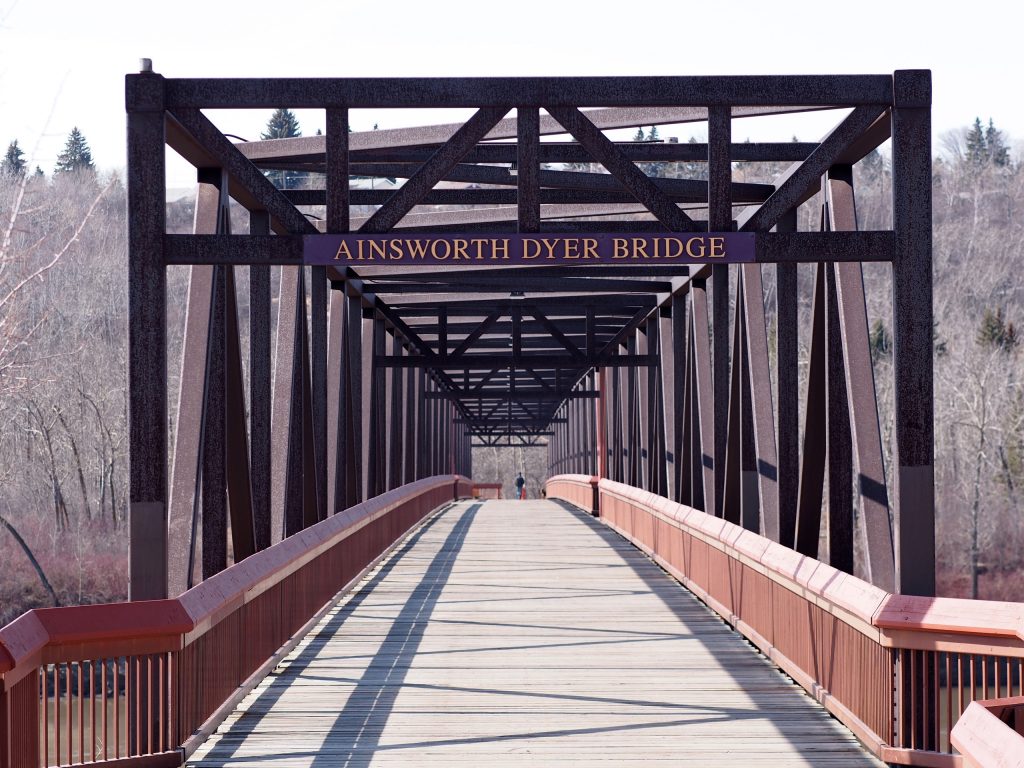 The entrance to a truss bridge with a plaque near the top of the structure labelled “Ainsworth Dyer Bridge”.