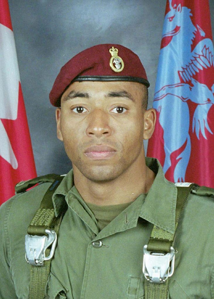 Corporal Ainsworth Dyer in a light green paratrooper uniform and a red beret.