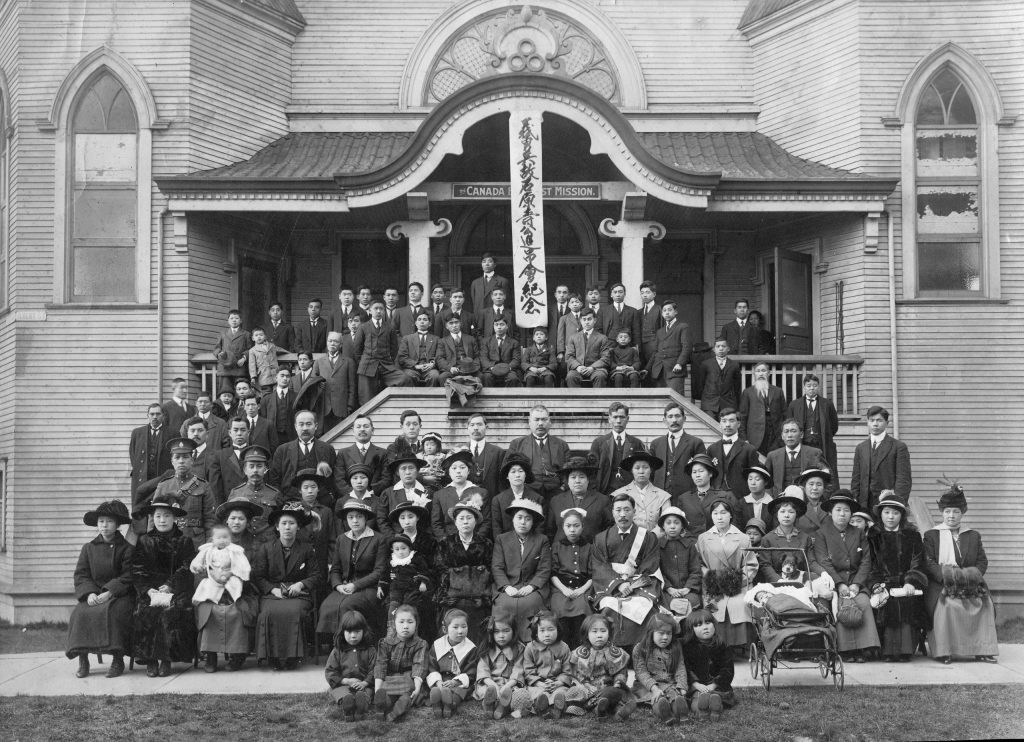 A large group of adults and children gathered beneath a long banner bearing Japanese characters.