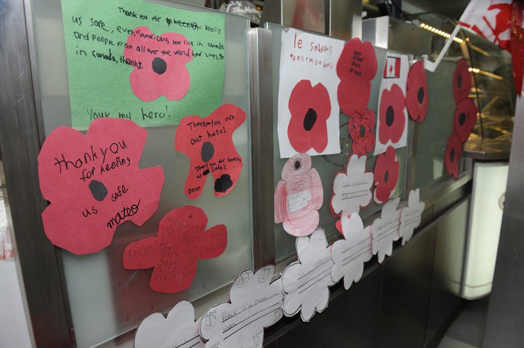 Paper poppies and handwritten French and English messages of thanks decorate the glass divider of a Tim Hortons restaurant service counter.