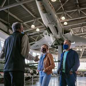 An interpreter speaking to two adults with a large military jet above them in the background