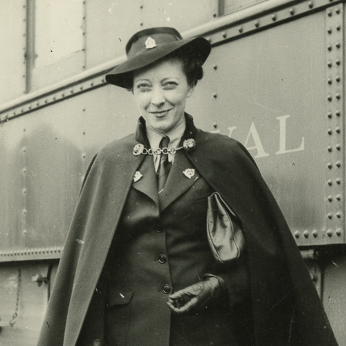 A woman in a cape standing next to a train at the Canadian War Museum.