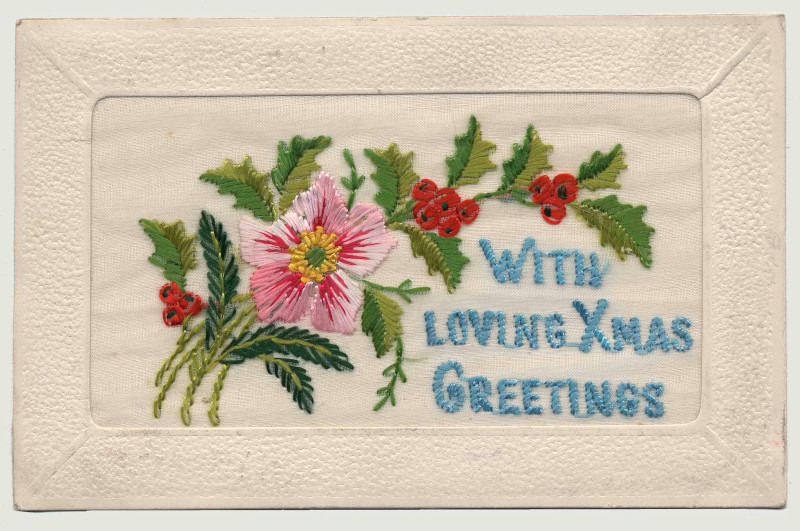 A rectangular piece of embroidery showing pink and red flowers with green leaves next to blue text reading “With Loving Xmas Greetings.”
