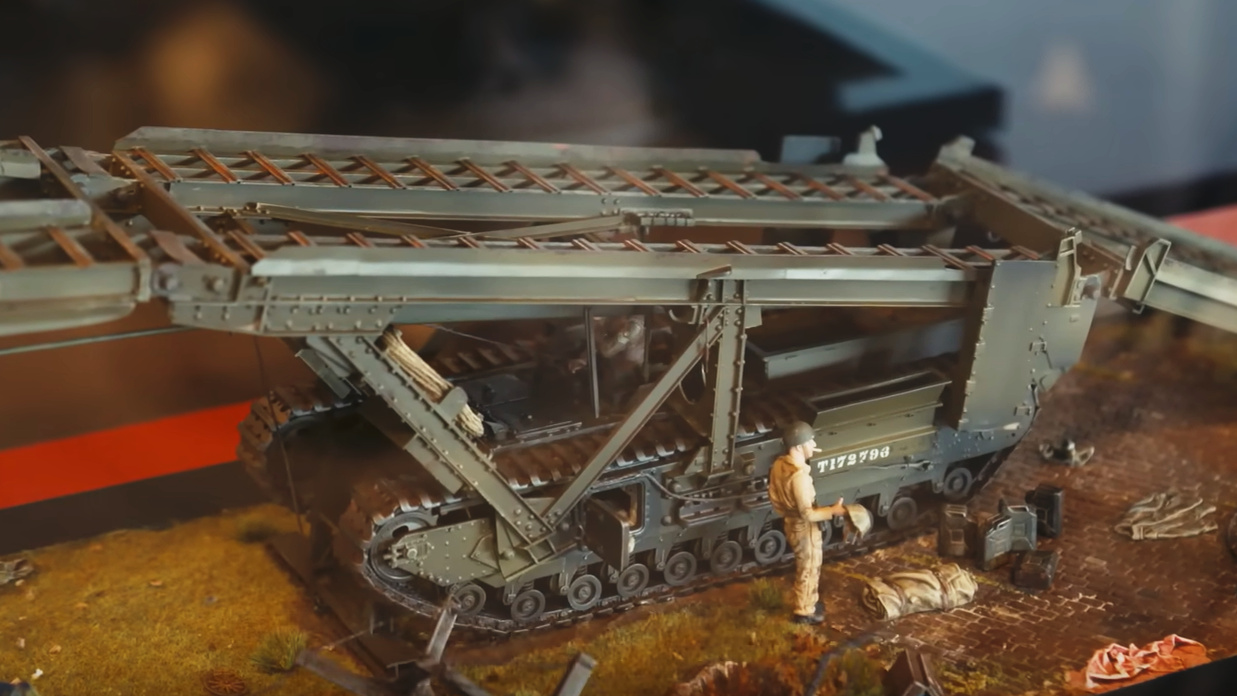 A scale model of a large, three-part, folding metal bridge mounted on a tracked military vehicle.