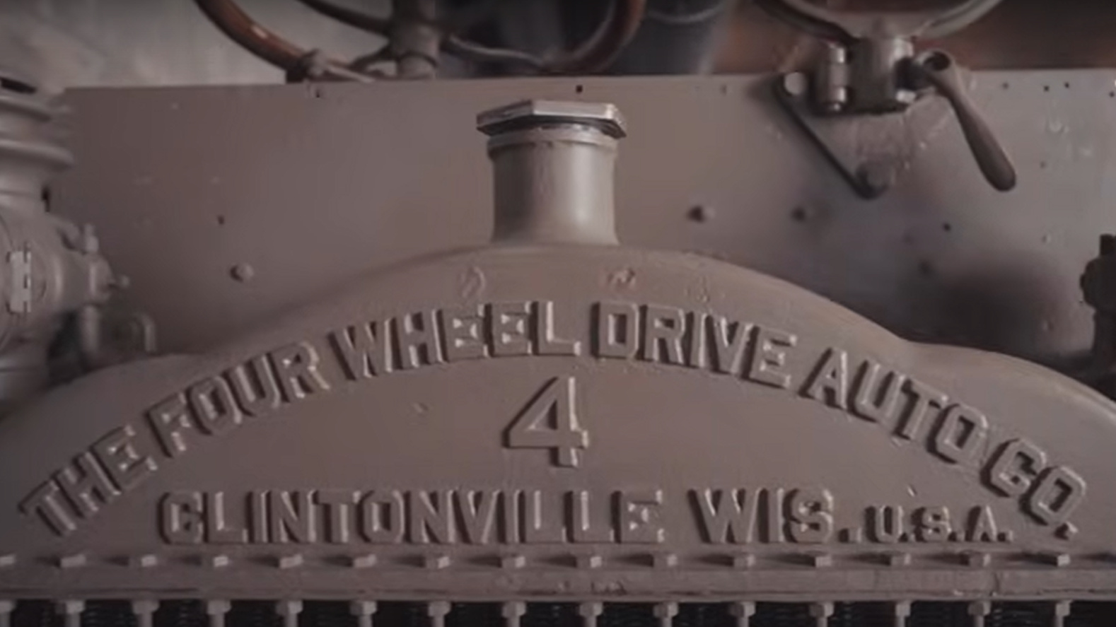 Close-up of the front of an old, grey, metal truck embossed with the words “The Four Wheel Drive Auto Ao., Clintonville, Wis., U.S.A.”