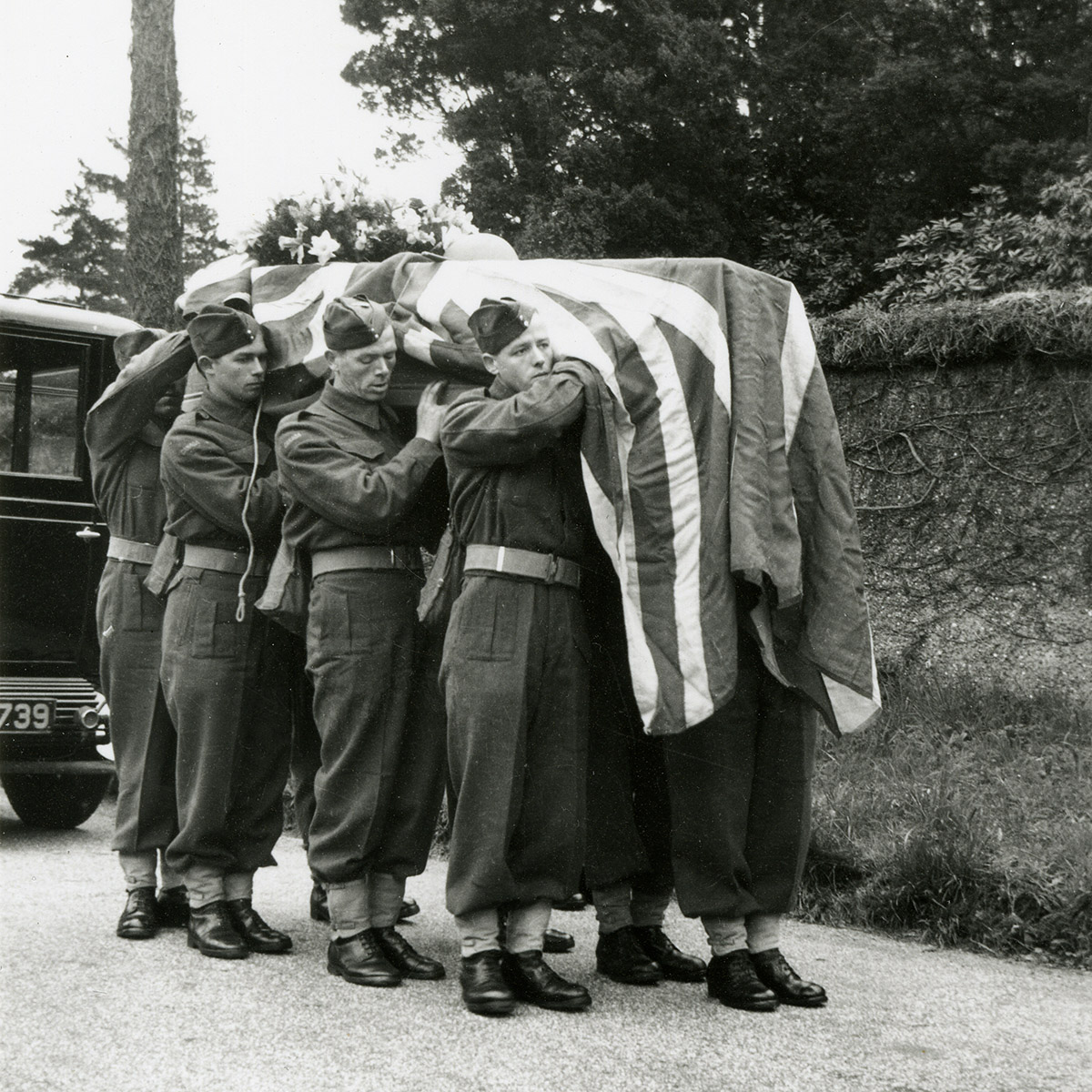 Photograph of eight soldiers carrying a flag-draped coffin on their shoulders.