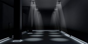 A darkened room illuminated by two rows of spotlights shining down from the ceiling and low strips of light along the bottom of the walls.