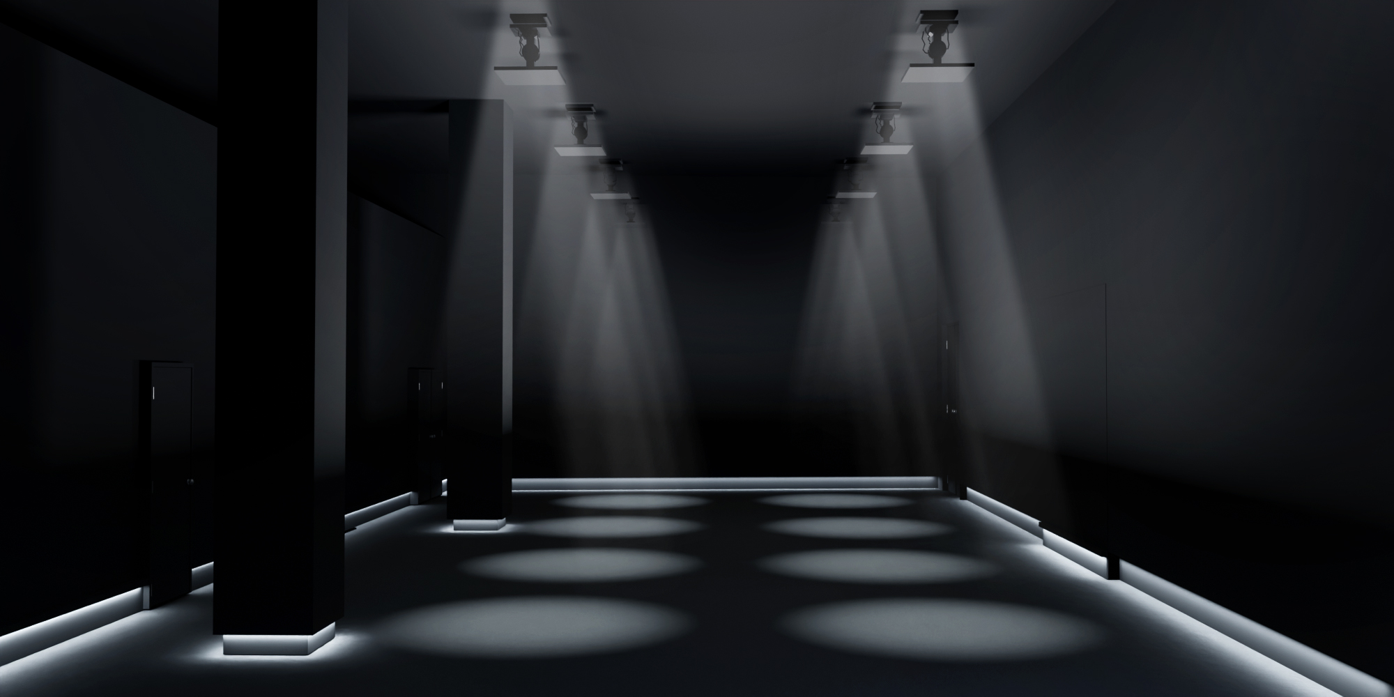 A darkened room illuminated by two rows of spotlights shining down from the ceiling and low strips of light along the bottom of the walls.