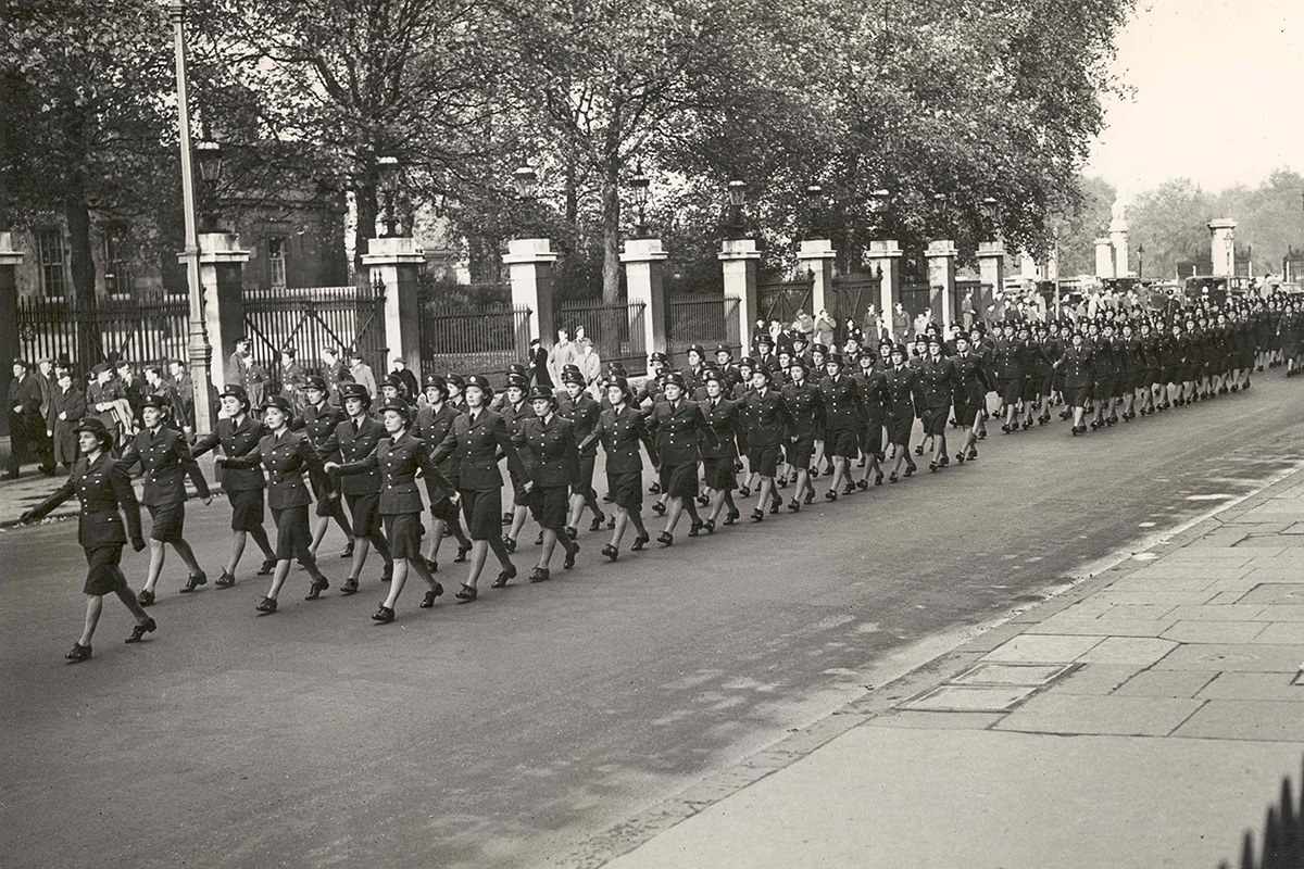 Photograph of a parade of women in uniform marching down the street, from right to left.