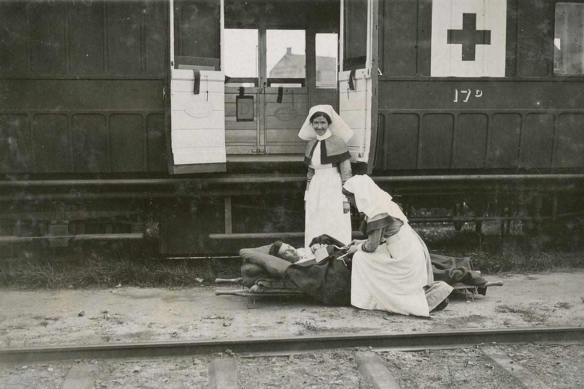 Photograph of two nurses in front of a hospital train attending to a person on a stretcher.