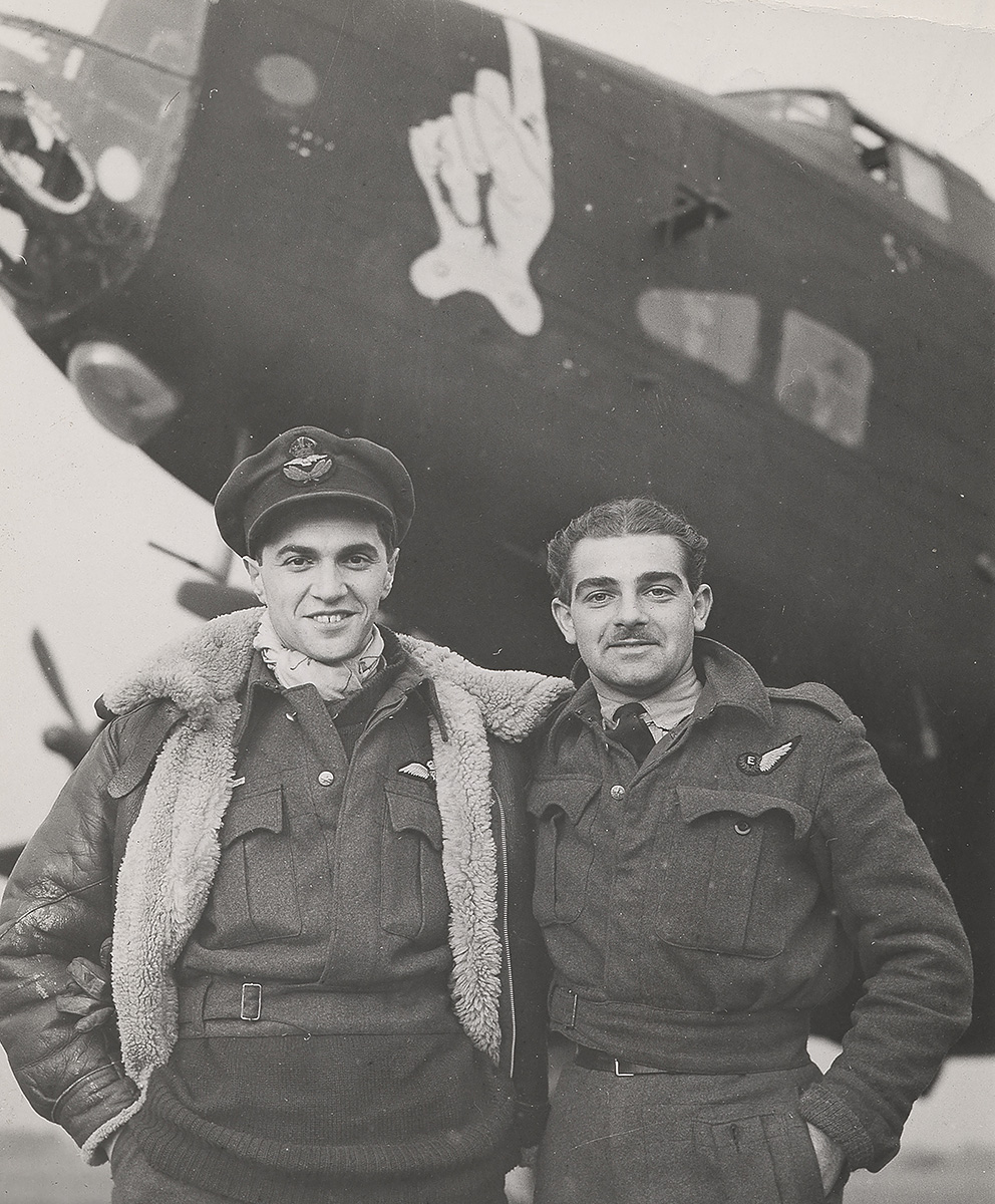 Photograph of two flight crew members standing in front of the nose of a Halifax bomber.