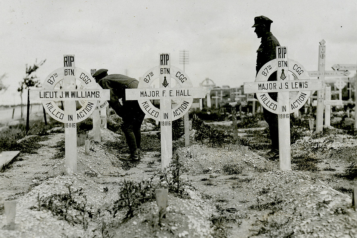 Photograph of soldiers looking at graves with white cross grave markers.