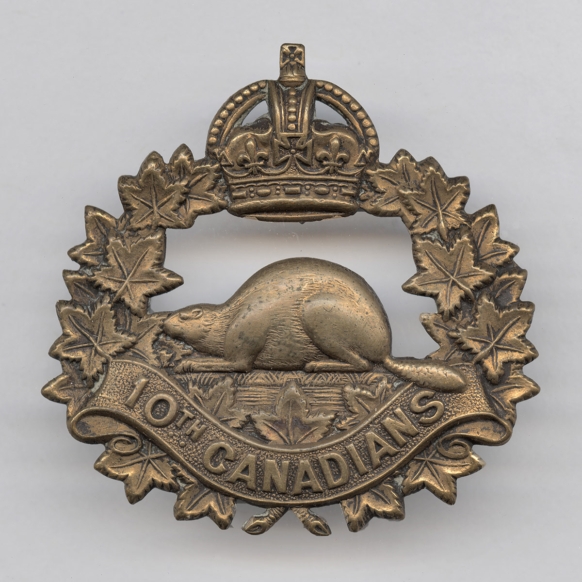 Metal cap badge with a wreath of maple leaves, a Tudor crown at the top, and a beaver in the middle. Reads: “10th Canadians.”