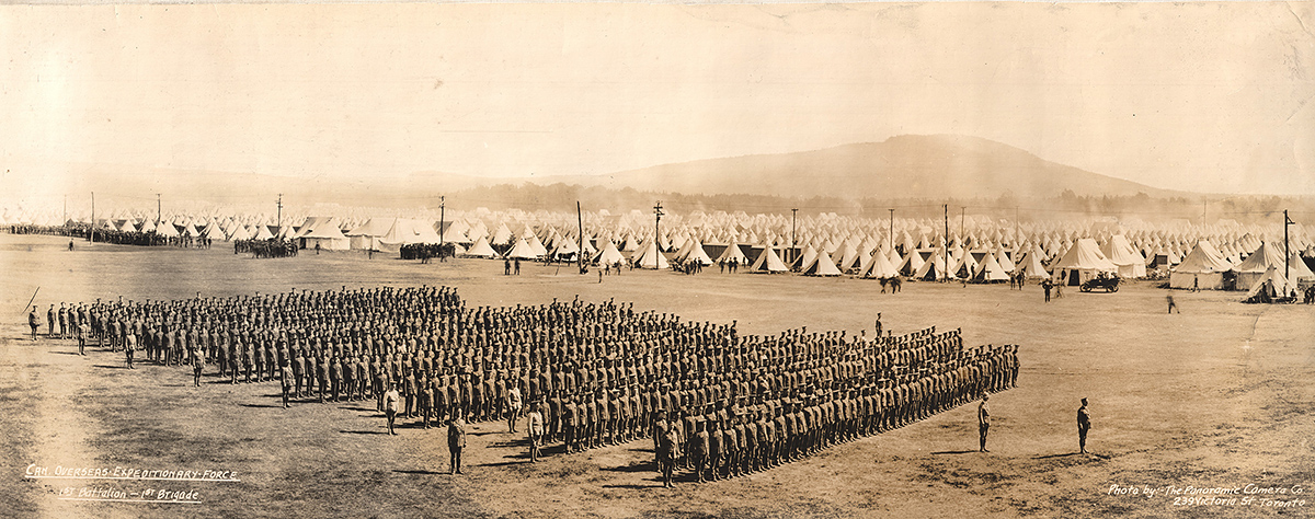Photograph of a battalion in parade formation in the foreground and a camp with many tents in the background.