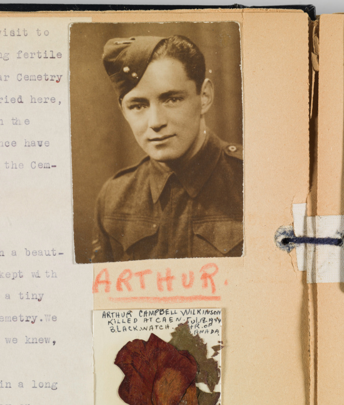 A photo of a young man in military uniform pasted into a scrapbook with a dried flower mounted on a card reading “Arthur Campbell Wilkinson. Killed in action at Caen July 18, 1944.”