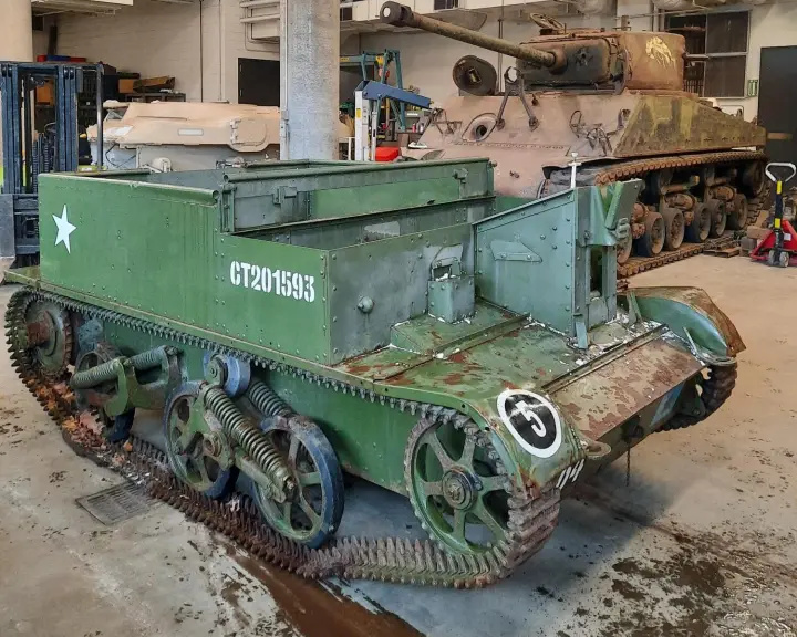 A low, boxy, green armoured vehicle with tracks. It has many patches of rust on its front end, tracks and wheels.