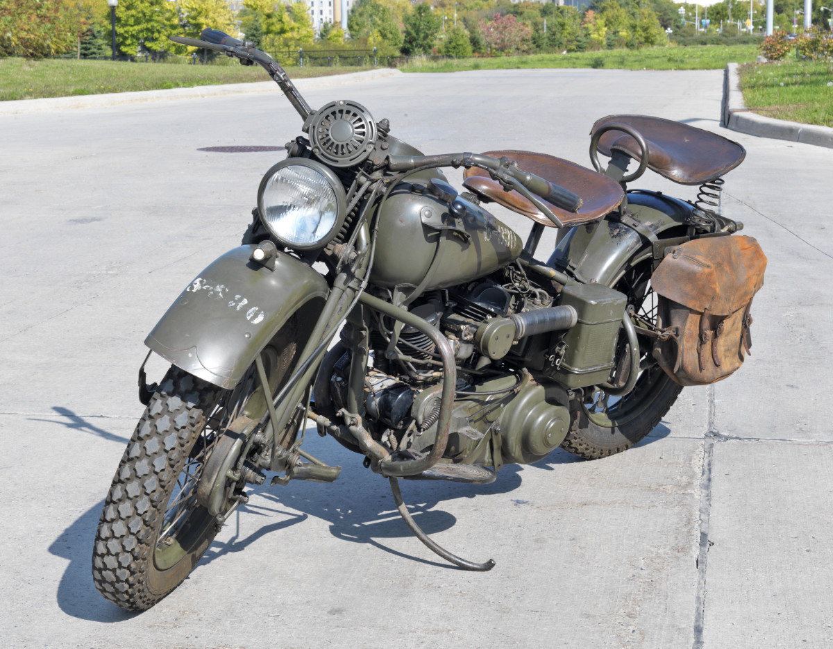 A dark green motorcycle with two large brown seats and a soft leather pannier.