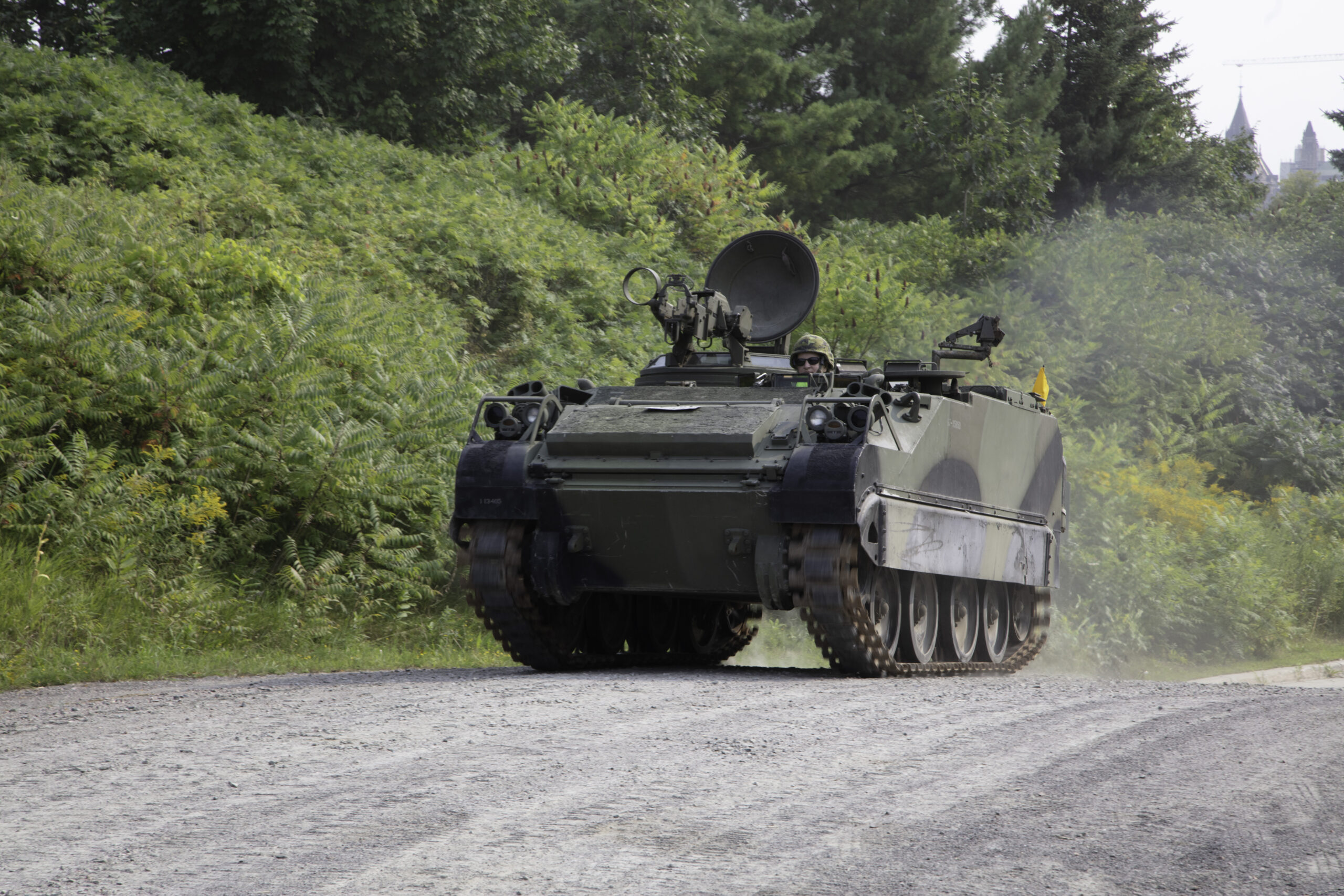 A tracked armoured vehicle in green, brown and black camouflage, with a communications dish antenna and a machine gun on top.