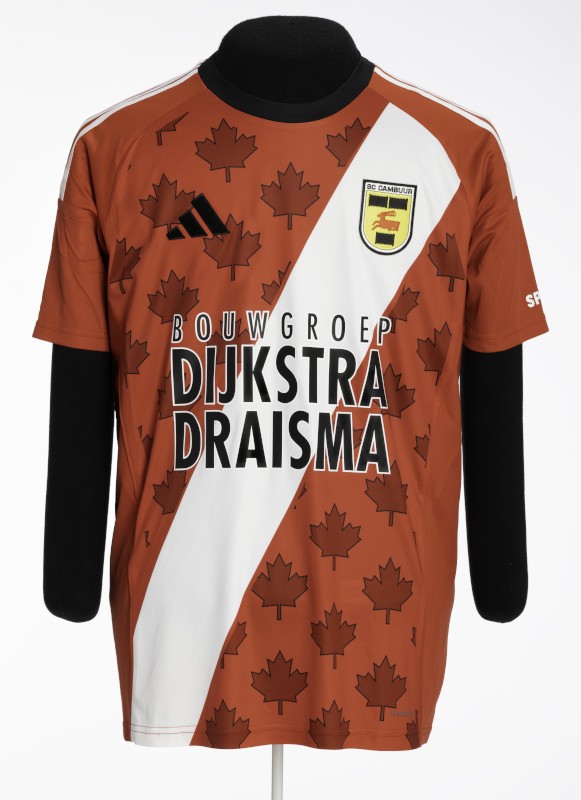 Orange-brown, short-sleeved athletic shirt covered with a repeating pattern of maple leaves, with a wide diagonal white stripe and large text reading “Bouwgroep Dijkstra Draisma.”