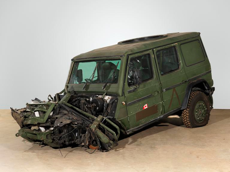 A green SUV-like vehicle missing its front wheels and with a smashed and crumpled front end and engine compartment