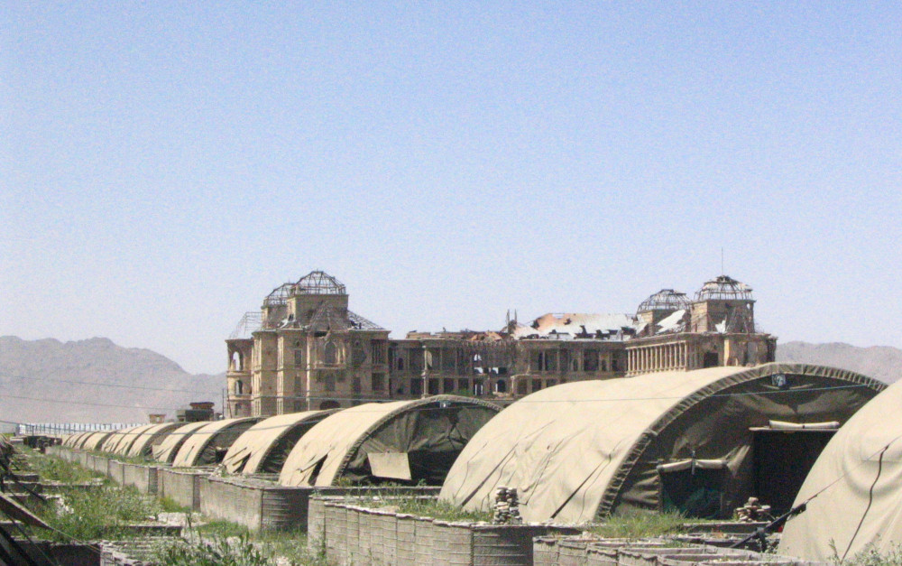 A long line of tent-like structures with curved roofs, with a large, ruined building in the background