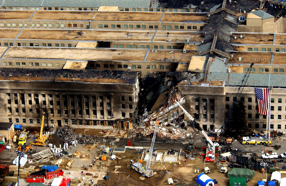 Aerial view of a large damaged and burned building with several construction vehicles working in the foreground.]