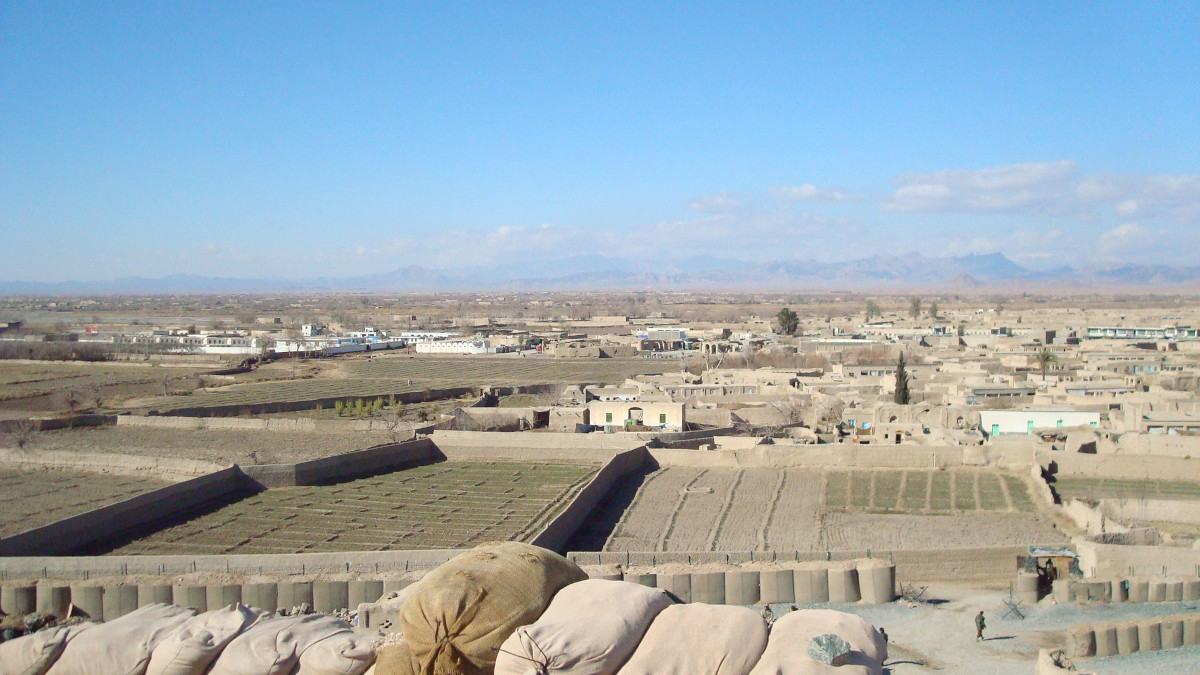 A flat landscape filled with low structures, compounds, and walls made of mud and concrete that extends far into the distance, with a low line of mountains just visible in the background.