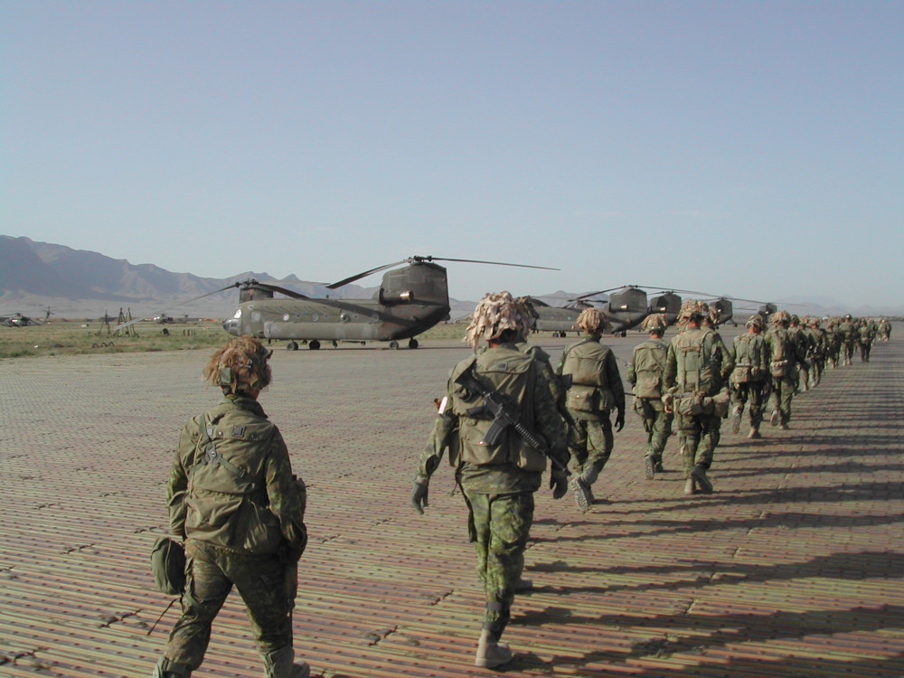 A long line of soldiers in green camo uniforms walk towards several large helicopters.