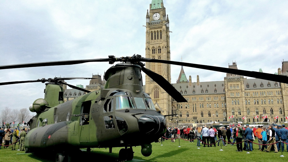 A large green helicopter and crowds of people in front of Canada’s Parliament buildings.