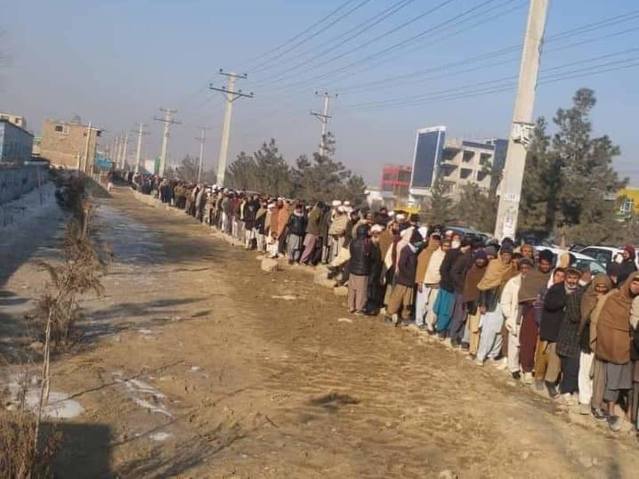 A very long line of people waiting at the side of a road.
