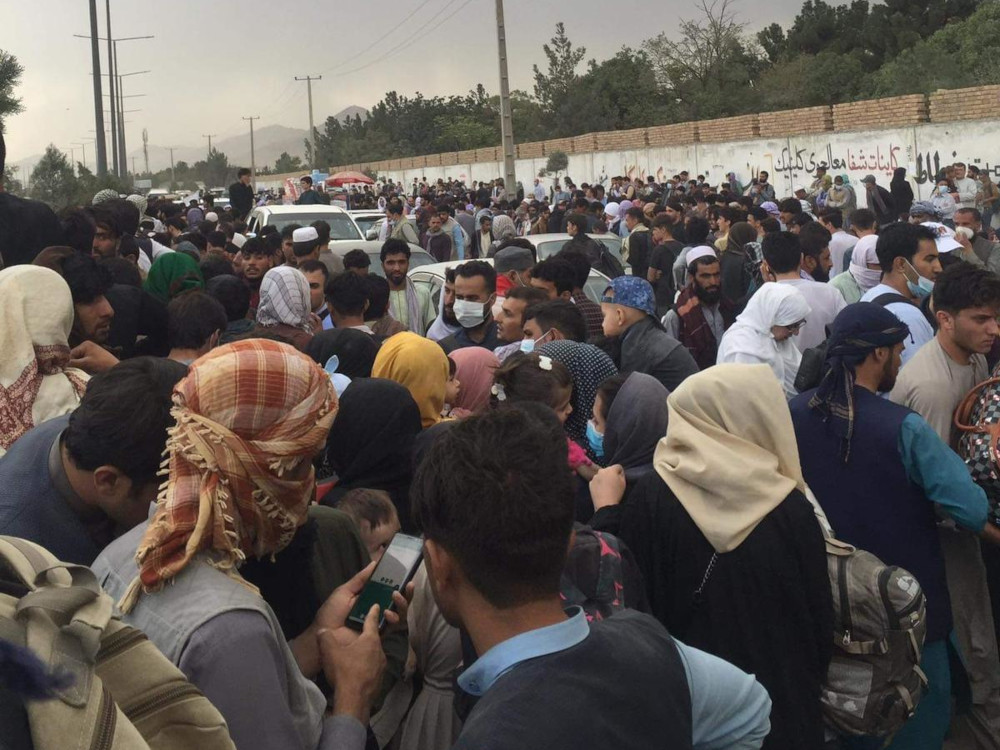 A large crowd of people with a long high wall in the background.