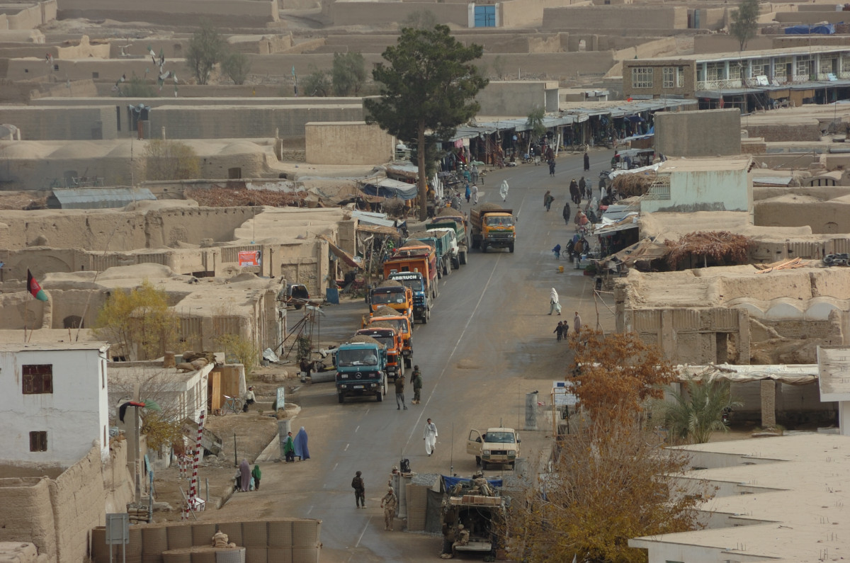 A street lined with low buildings, vehicles and people.