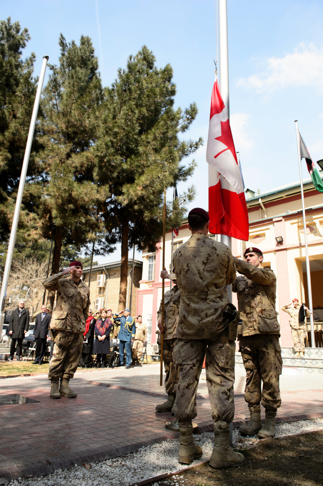 Two soldiers lower a Canadian flag as a third soldier salutes.