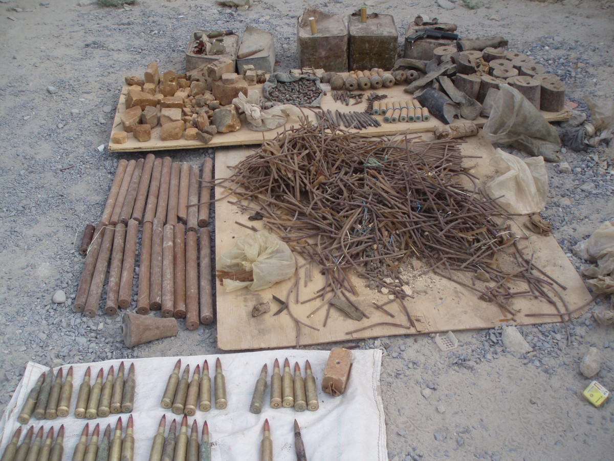 A collection of ammunition and scraps of metal of various sizes spread out on the ground, on sheets of wood and cloth.